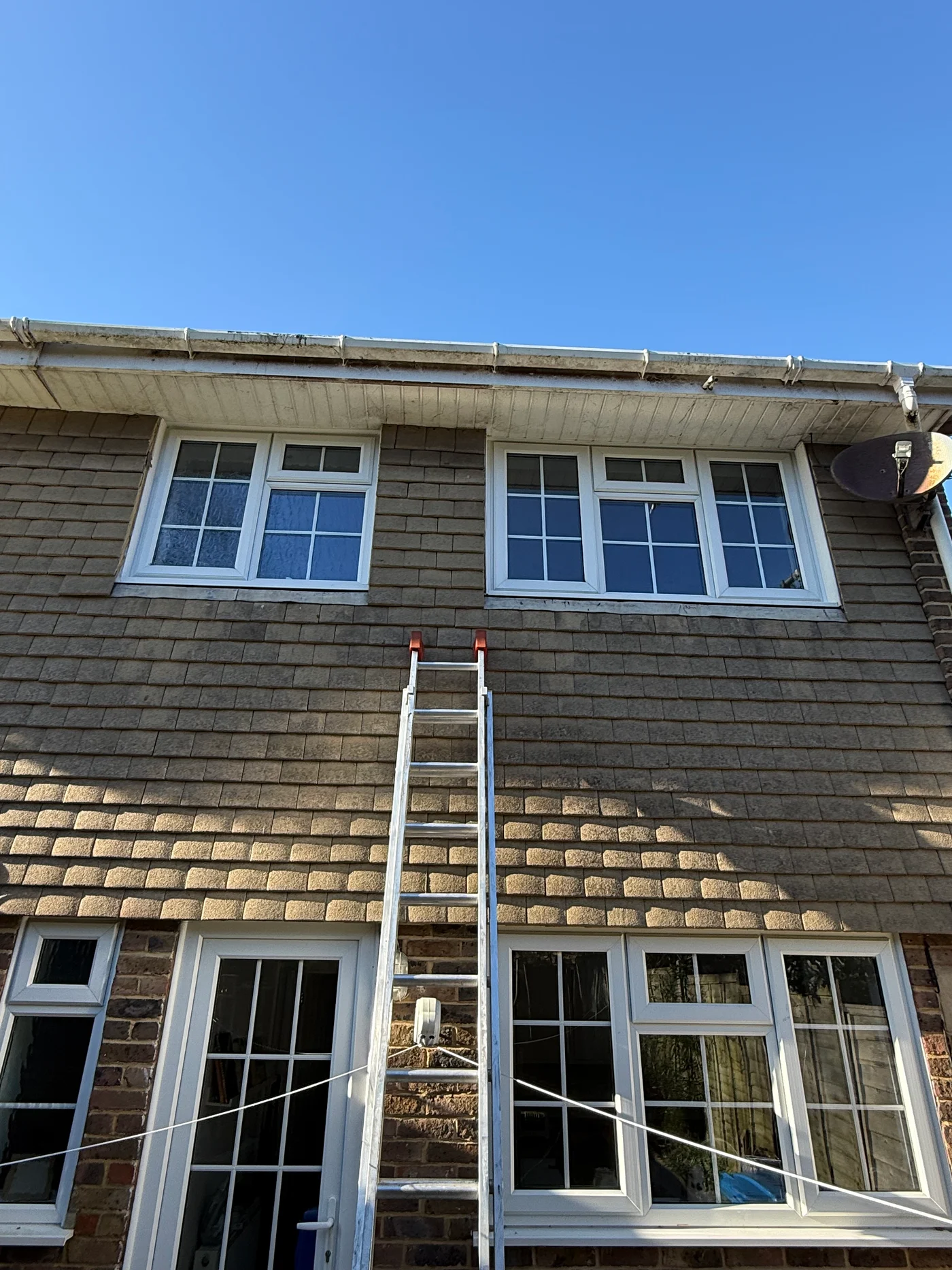 House elevation with a stained, algae-covered fascia and gutter before cleaning, ladder in position
