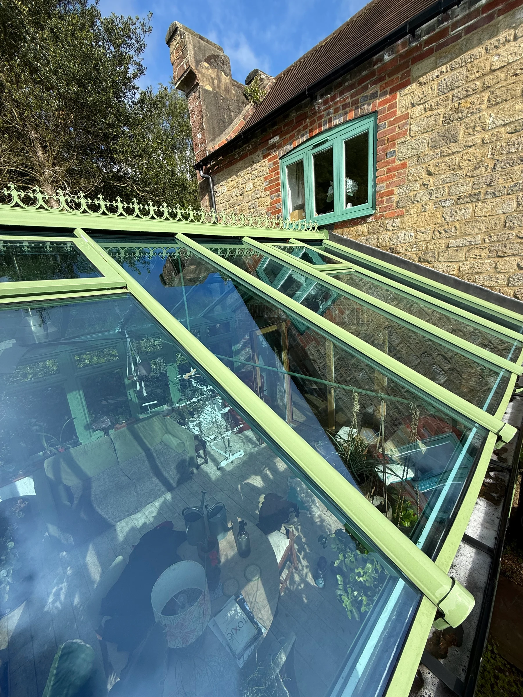 Close-up of a green-framed conservatory glass roof and decorative ridge cresting from below