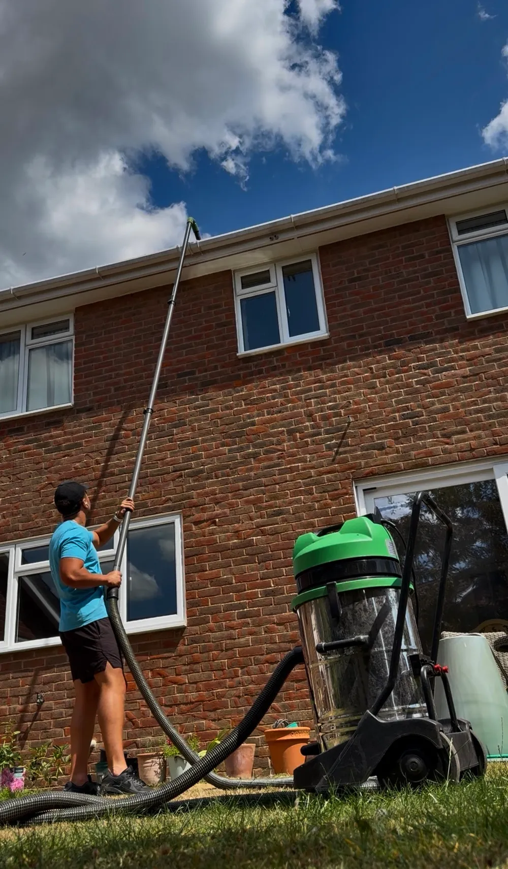 GWC operative reaching a roofline gutter with a telescopic vacuum pole, vacuum unit on the ground below