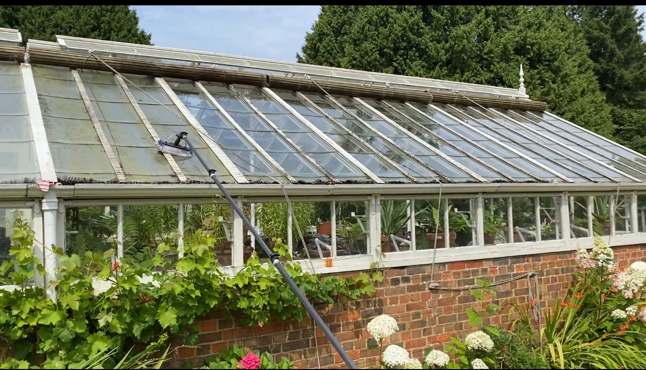 Grant's Window Cleaning operative cleaning the glass of a large Victorian greenhouse with a water-fed pole